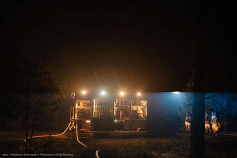 Zdjęcie przedstawiające nocne działania gaśnicze strażaków przy pożarze dachu, z widocznym oświetleniem miejsca zdarzenia