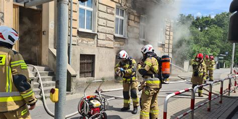 Zdjęcie przedstawiające akcję gaśniczą straży pożarnej przy kamienicy z widocznym dymem wydobywającym się z poddasza