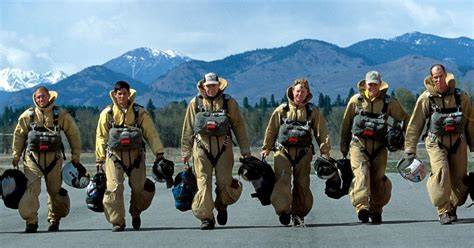 zdjęcie przedstawiające strażaków typu smokejumpers (fire jumpers) skaczących ze spadochronami w stronę płonącego lasu