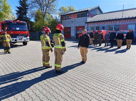 zdjęcie strażaków OSP Budzów w pełnym umundurowaniu stojących przed remizą