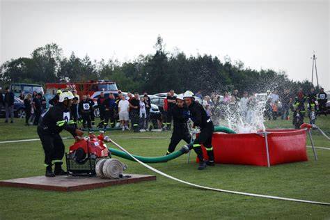Strażacy podczas zawodów sportowo-pożarniczych, w tle sprzęt pożarniczy