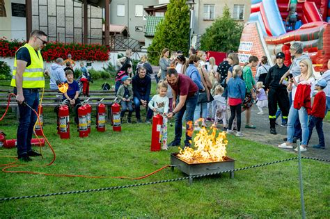 Tematyczne zdjęcie przedstawiające piknik strażacki z widocznymi atrakcjami i uśmiechniętymi ludźmi