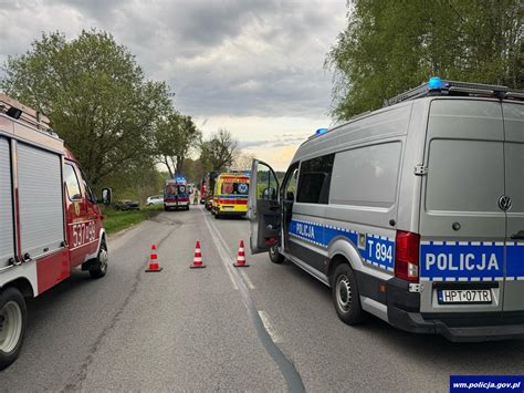 Wóz strażacki i policja na miejscu zdarzenia drogowego z płonącym pojazdem, widoczne korki