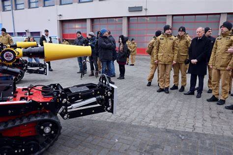 Tematyczne zdjęcie robota gaśniczego w akcji z widocznym dymem i strażakami w tle