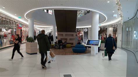 zdjęcie wnętrza galerii handlowej z widocznym tłumem ludzi i opuszczonymi roletami zabezpieczającymi