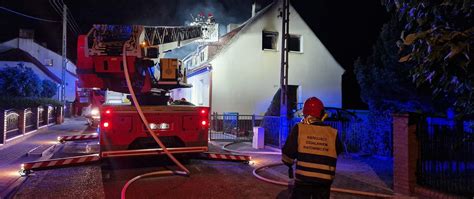 Zdjęcie strażaków gaszących pożar budynku mieszkalnego w nocy, z widocznymi wozami strażackimi i dymem