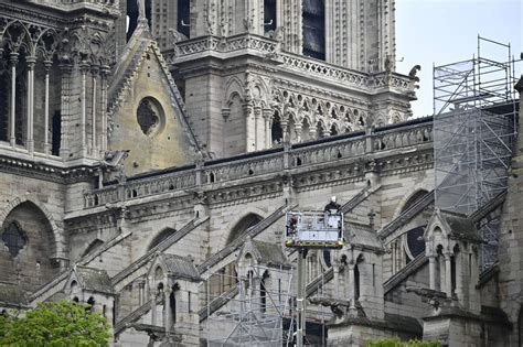 Zbliżenie na zniszczony dach katedry Notre-Dame po pożarze, ukazujące wypalone belki konstrukcyjne i otwory w sklepieniu.