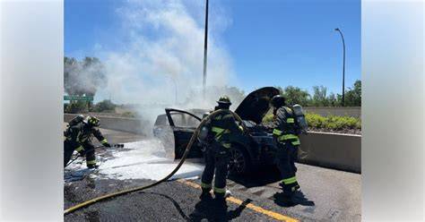 Car fire on a road, with firefighters present