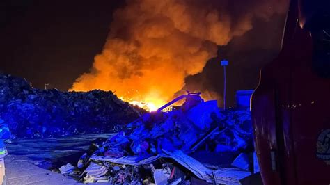 Zdjęcie strażaków gaszących pożar na składowisku odpadów, ukazujące trudności terenu