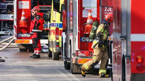 Zdjęcie przedstawiające strażaków w trakcie akcji chłodzenia butli z gazem, z widocznym dymem i uszkodzoną konstrukcją wiaty