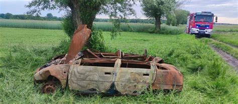 wypalony wrak samochodu osobowego na parkingu, w tle inne pojazdy