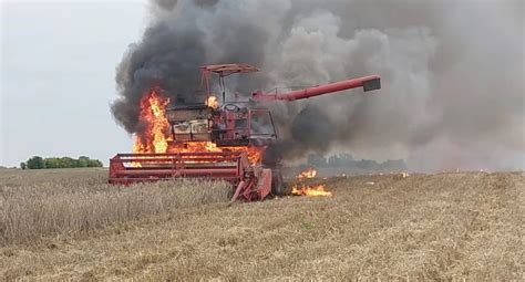 Zapalony kombajn na polu podczas żniw, strażacy gaszący ogień
