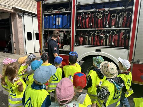 Grupa dzieci zwiedza remizę strażacką, oglądając sprzęt i pojazdy pożarnicze.