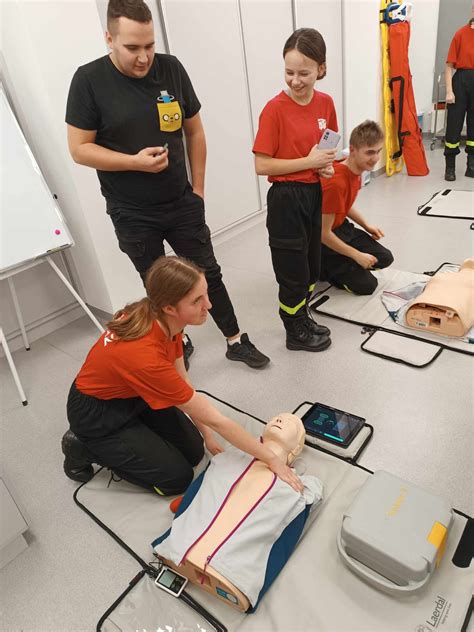 Zdjęcie grupy osób uczestniczących w szkoleniu z pierwszej pomocy, ćwiczących resuscytację na fantomie.