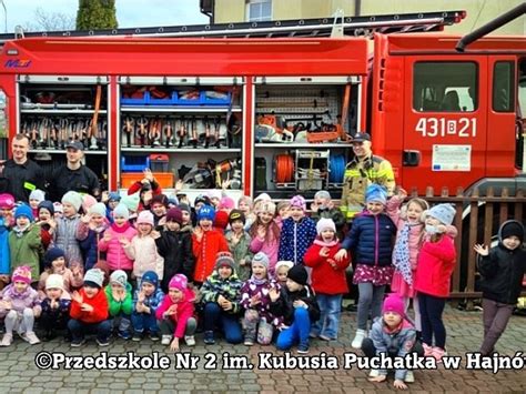 grupa przedszkolaków z uśmiechniętym strażakiem i wozem strażackim